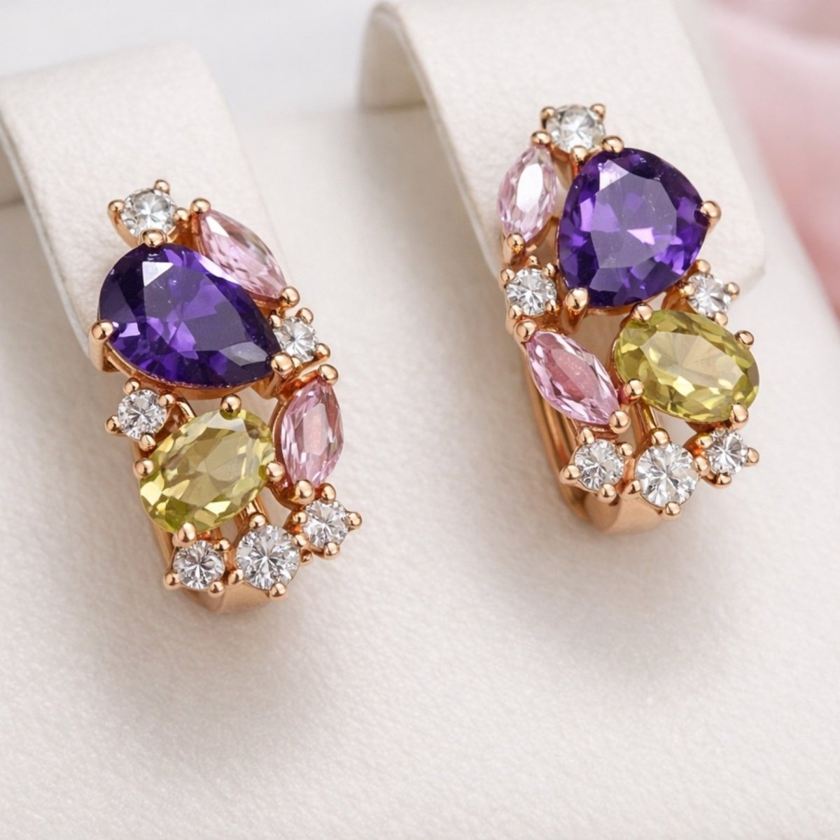 A pair of Kouvr Vanya multi-gemstone cluster earrings in 14K rose gold, featuring purple amethyst, green peridot, and pink tourmaline, shown on a white jewelry display stand.