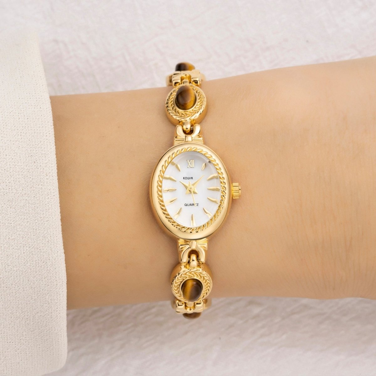 White Gold kouvr wristwatch with white face on a wrist against a light background