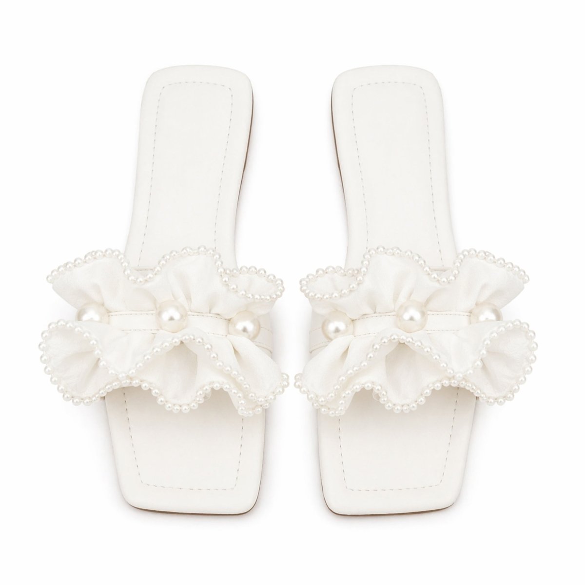 Top-down view of a pair of Kouvr Vionnet white flat slide sandals with satin ruffles and pearl details on a white background.