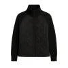Woman wearing the Kouvr Fashion black quilted jacket with cable knit sleeves and a funnel neck collar, styled for a casual city look