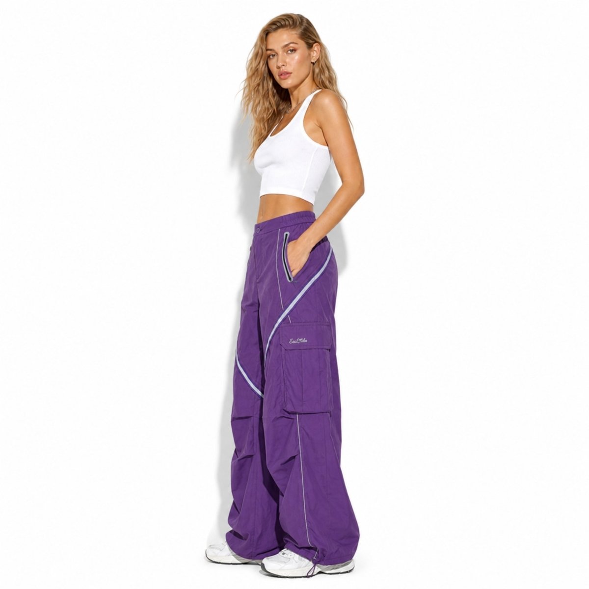 Side profile of fashion model in deep purple nylon cargo track pants showing large side utility flap pockets, zipper details, and adjustable toggle hem styling.