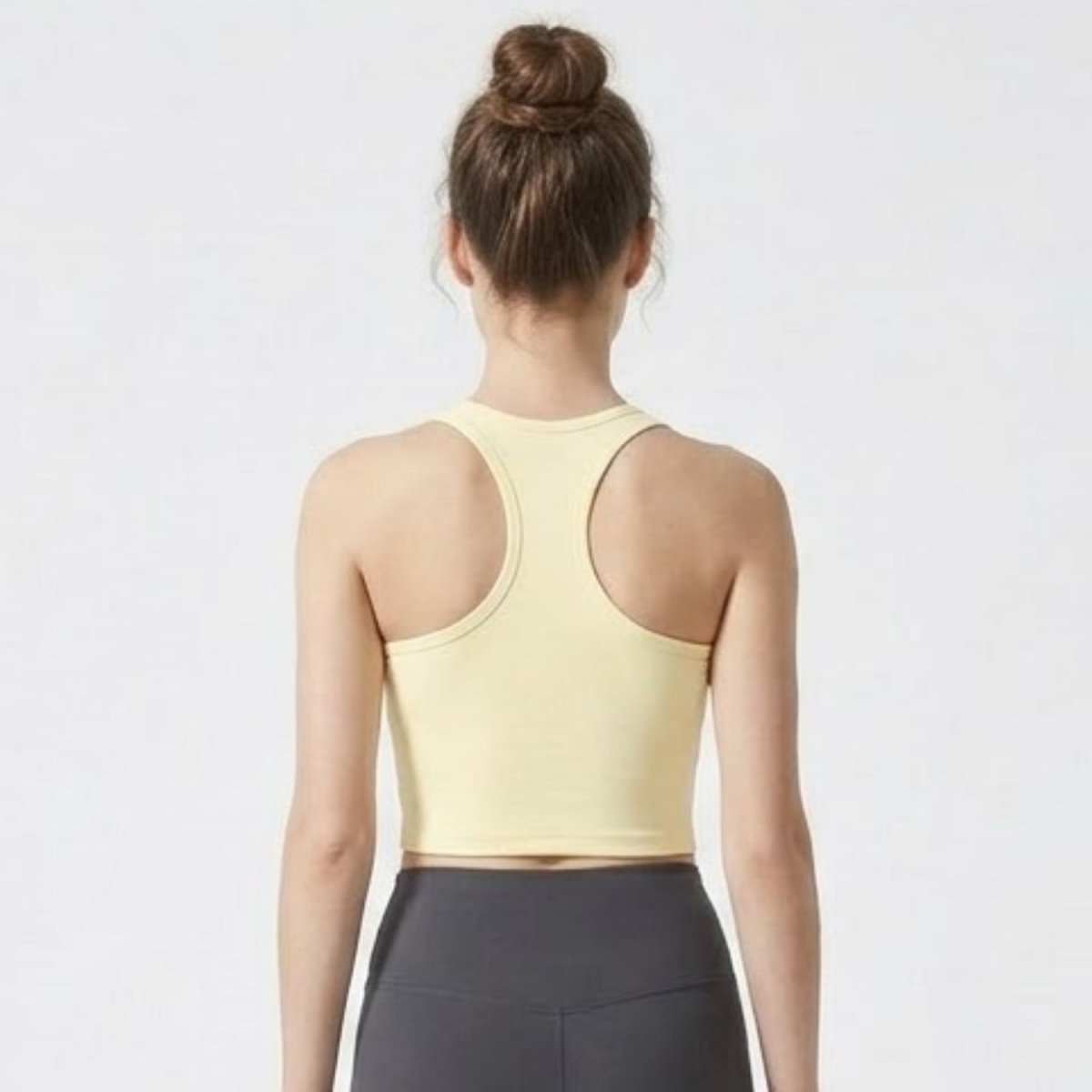 Back view of woman wearing Kouvr butter yellow racerback workout crop top showing shoulder blade contour