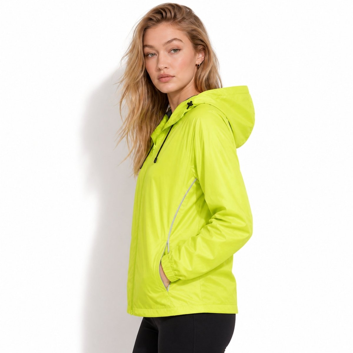 Side profile of female model wearing Kouvr yellow lightweight hooded rain shell with reflective piping