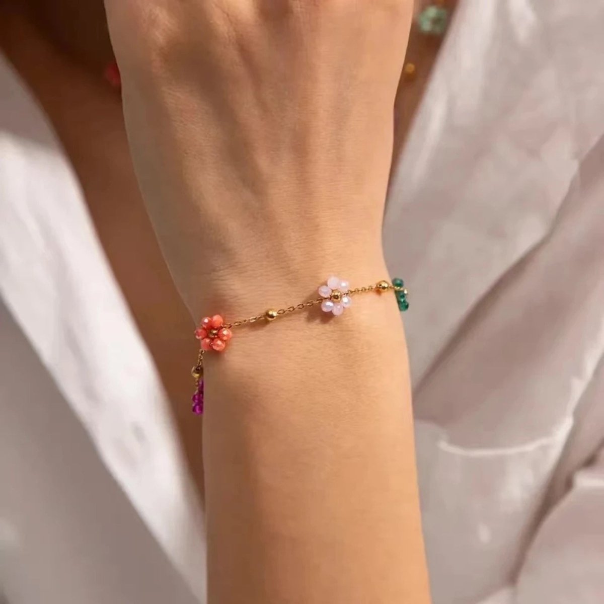 Close-up of the Kouvr Ysabel set beaded flower bracelet on a woman's wrist, showcasing the pink, white, and green beaded flowers on the gold chain.
