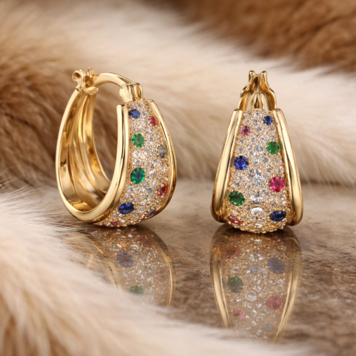 A detailed lifestyle shot of the Kouvr Yvette gold hoop earrings resting on a reflective surface with a soft fur background, highlighting their sparkle and craftsmanship.