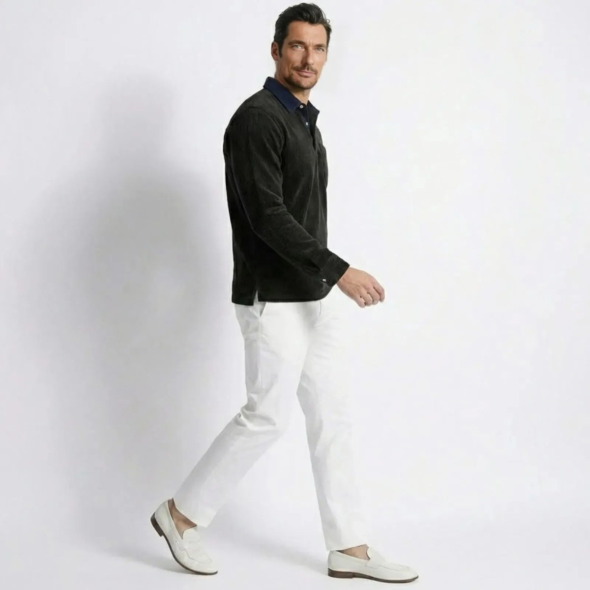 Side profile of a man walking while wearing the Kouvr Zain Black Corduroy Polo, showcasing its fit and silhouette.
 