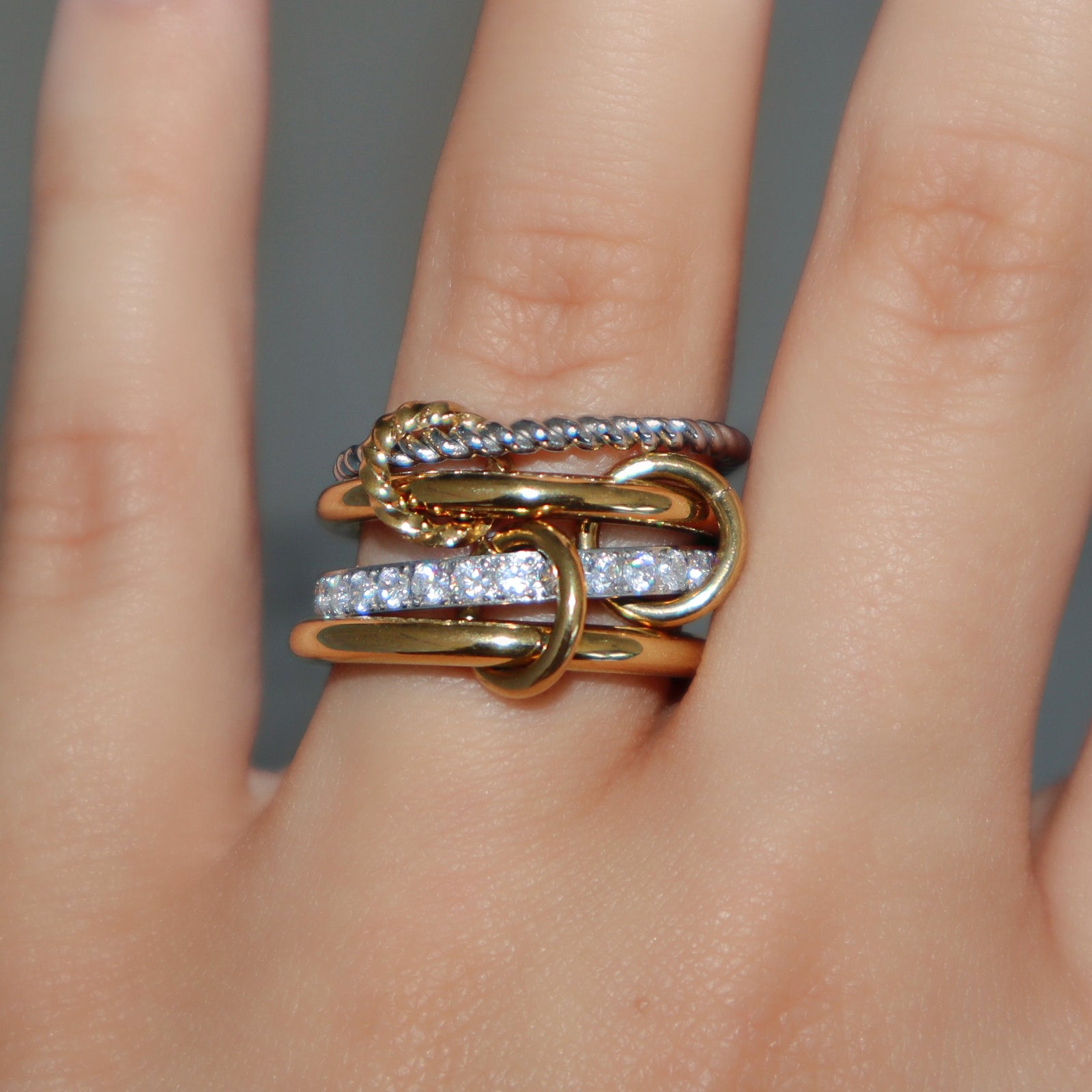 Kouvr Zeina interlocking stacked ring in 18k two-tone gold with pavé diamonds shown on a woman's finger.
