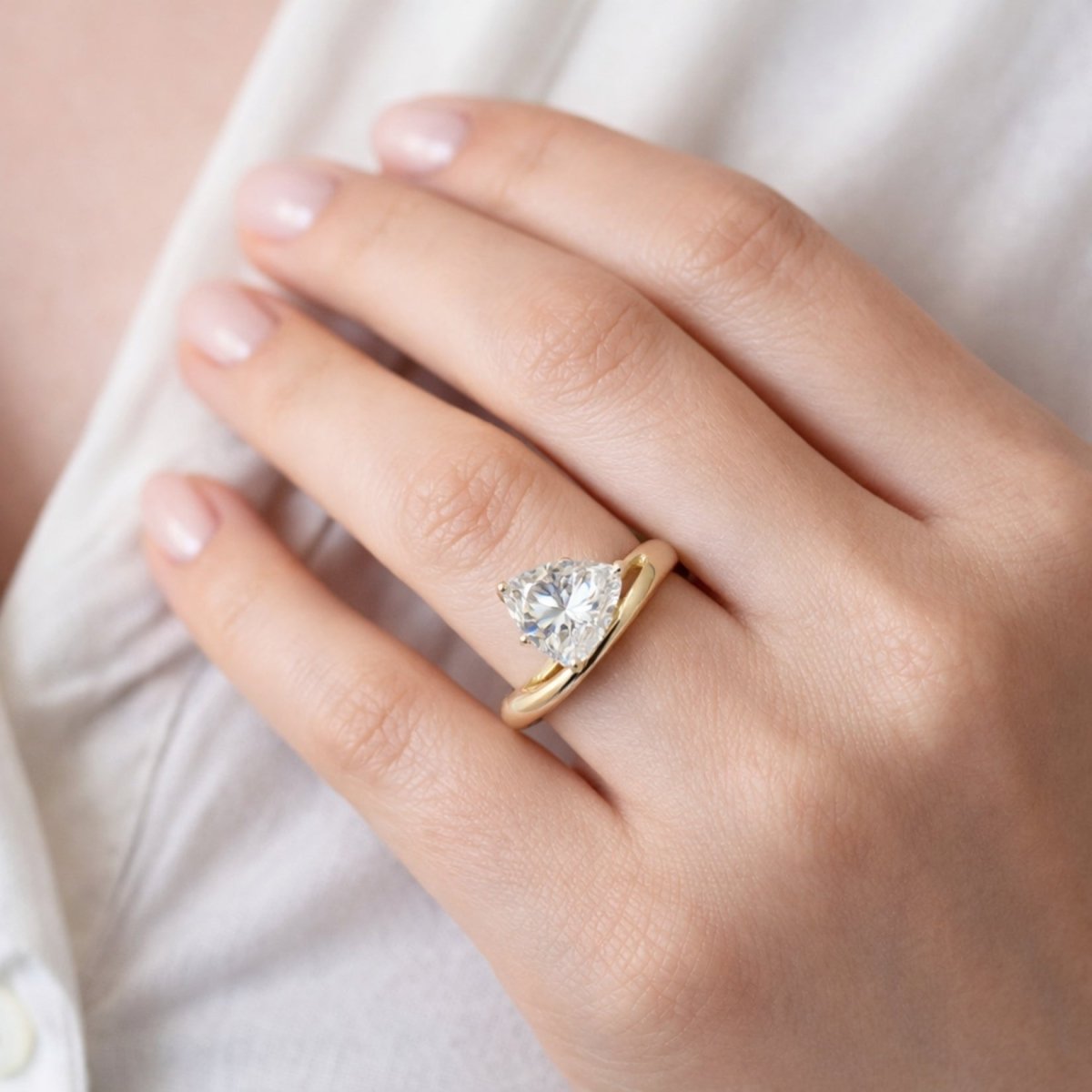 A close-up view of the Kouvr Zella pear cut engagement ring on a woman's hand, showing the unique gold bypass wave design.