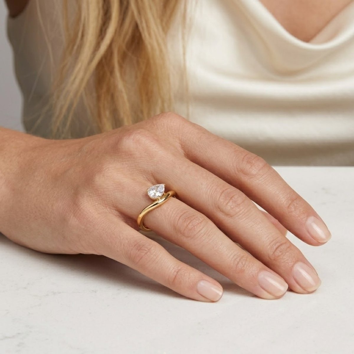 A model's hand wearing the Kouvr Zoella heart shaped diamond bypass ring in 18k yellow gold.