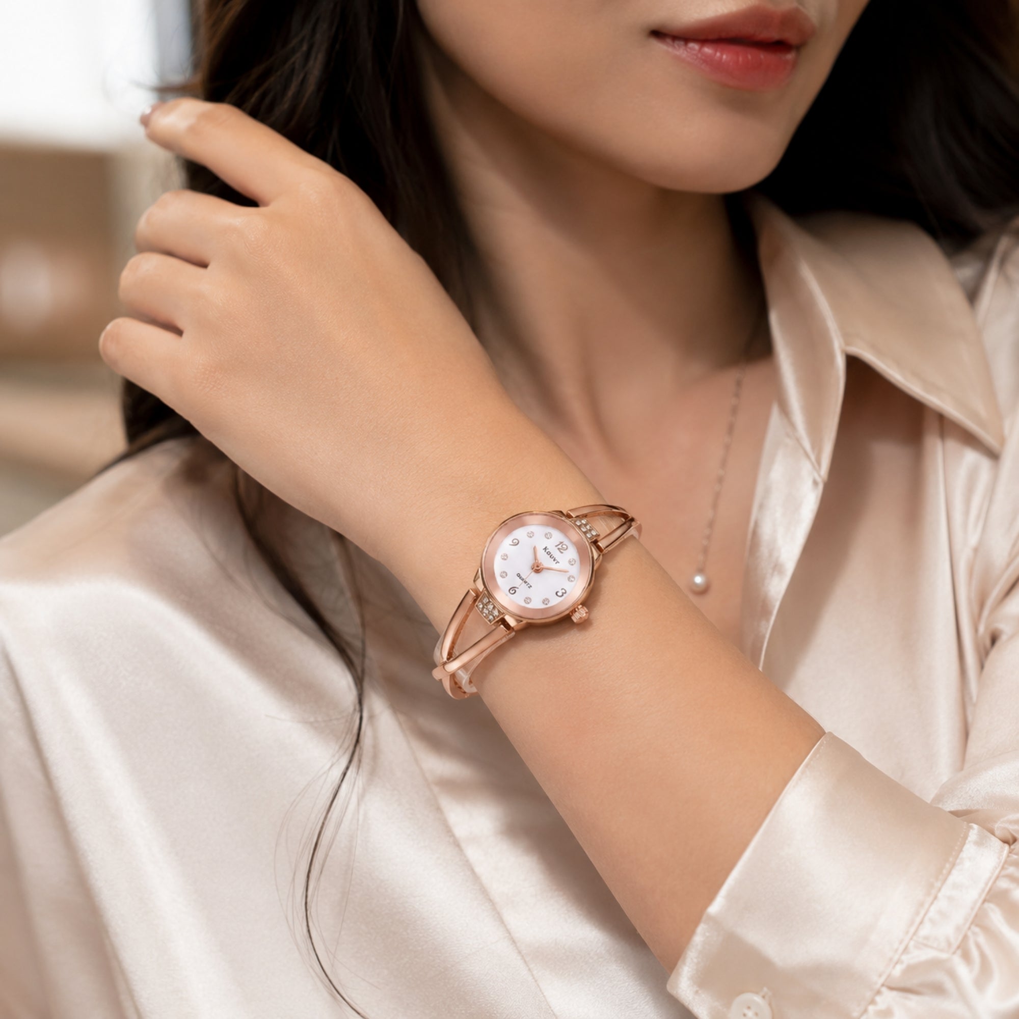 Close up of a woman elegantly styling the Kouvr rose gold criss cross bangle watch with a silk blouse for elevated everyday wear.