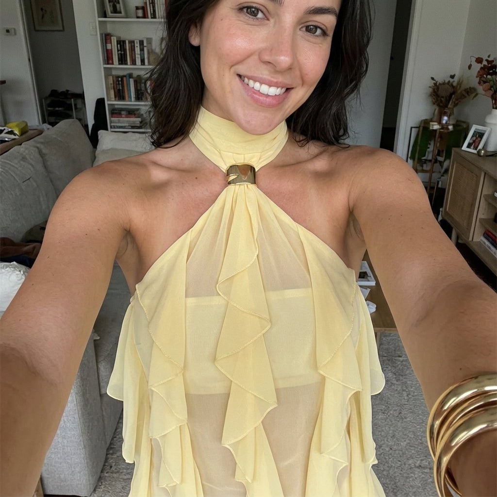 Casual mirror selfie of woman smiling while wearing the pale yellow flowy halter top with a bandeau underneath.