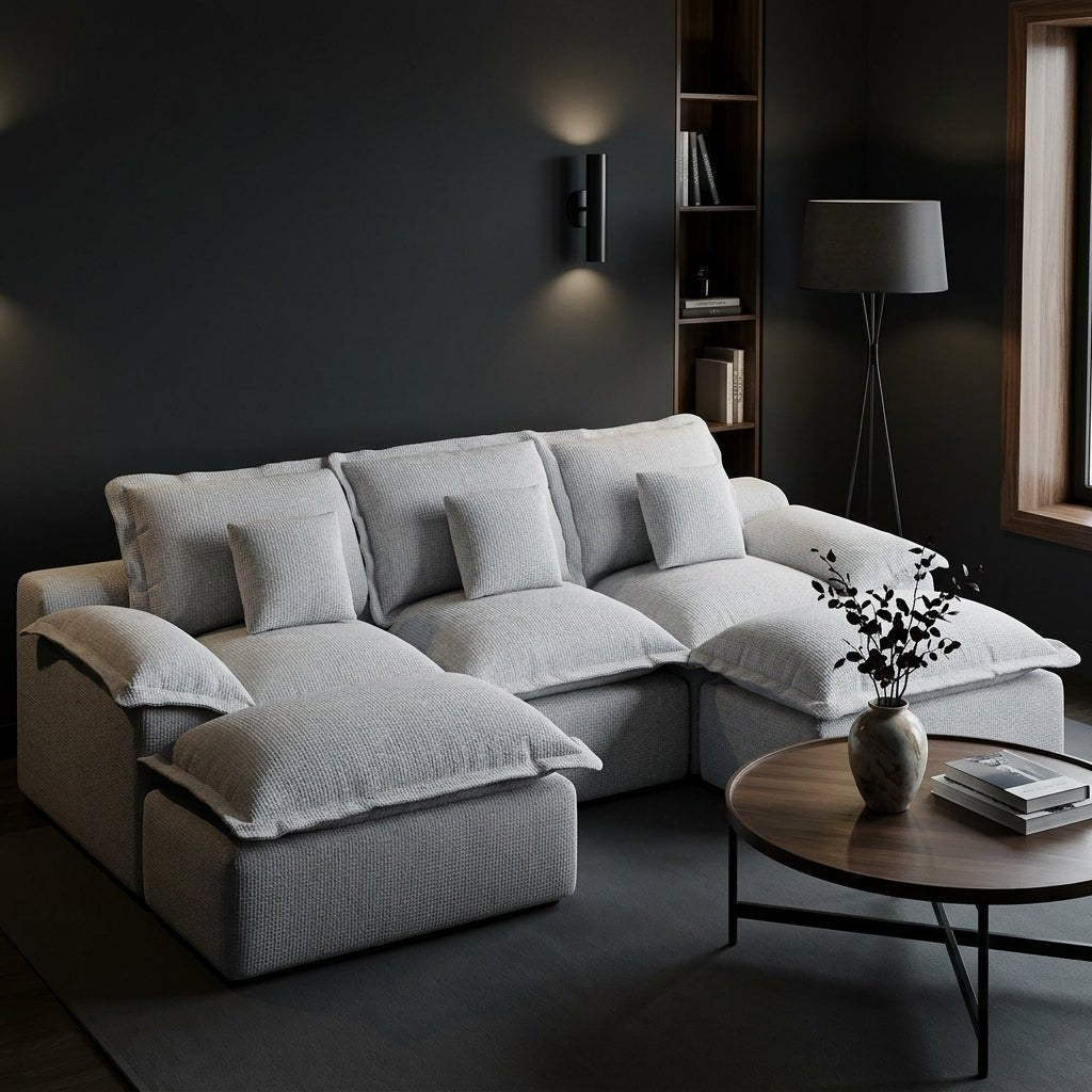 Symmetrical front view of a light grey U-shaped pit sofa with plush cushions on a neutral textured rug against a white wall.