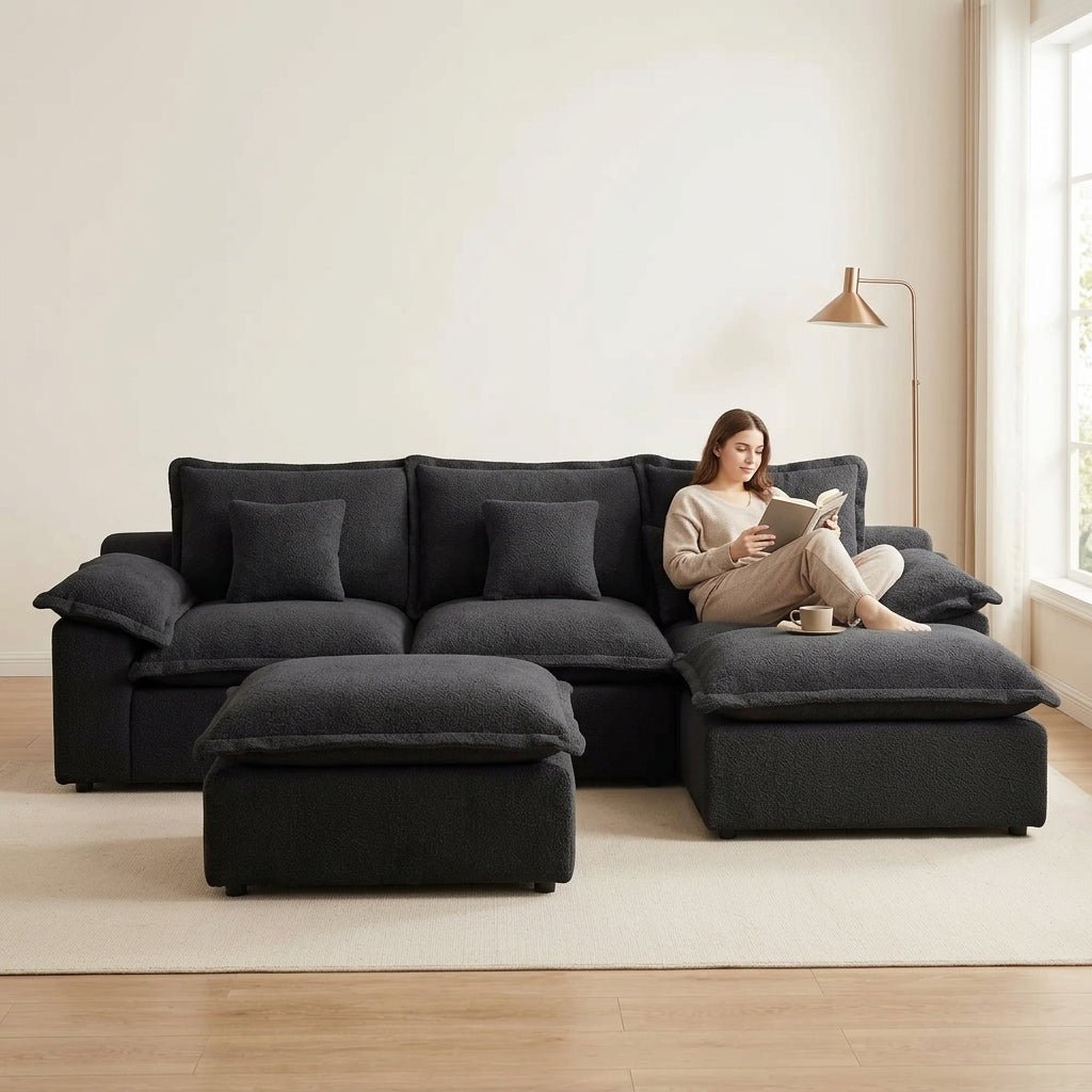 Modern low-profile black sectional sofa in a minimalist room featuring a natural wood side table and indoor plant.