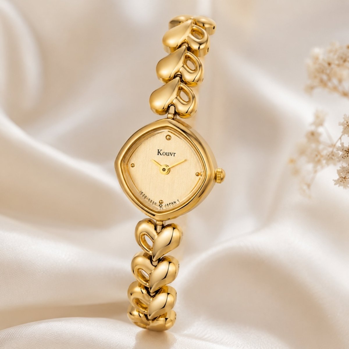 Close up of the Kouvr gold elegant women's watch resting beautifully on soft, folded white silk fabric with delicate dried floral accents.
