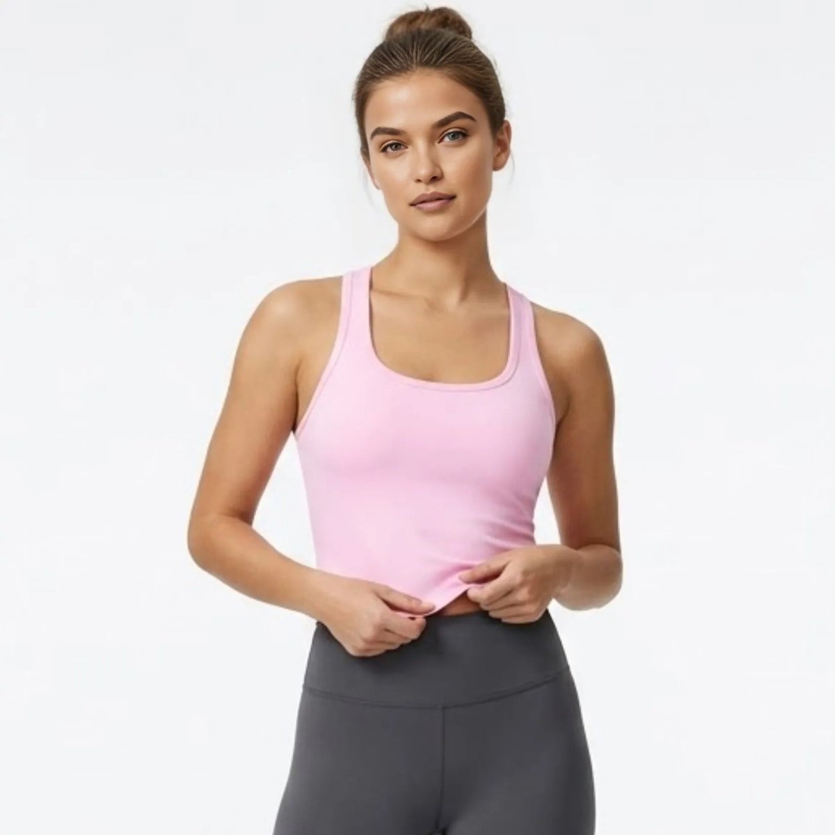 Front view of female model wearing Kouvr luxury pink racerback crop top and dark grey high-waisted leggings