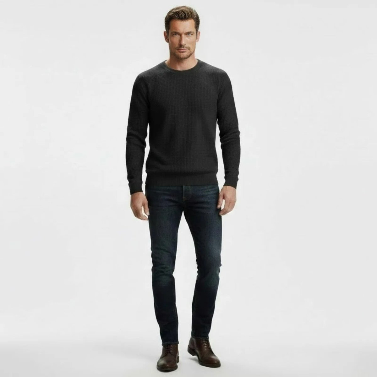 Man wearing a slim fit dark grey waffle knit crewneck sweater from Kouvr Fashion, paired with dark wash jeans and brown leather shoes.
