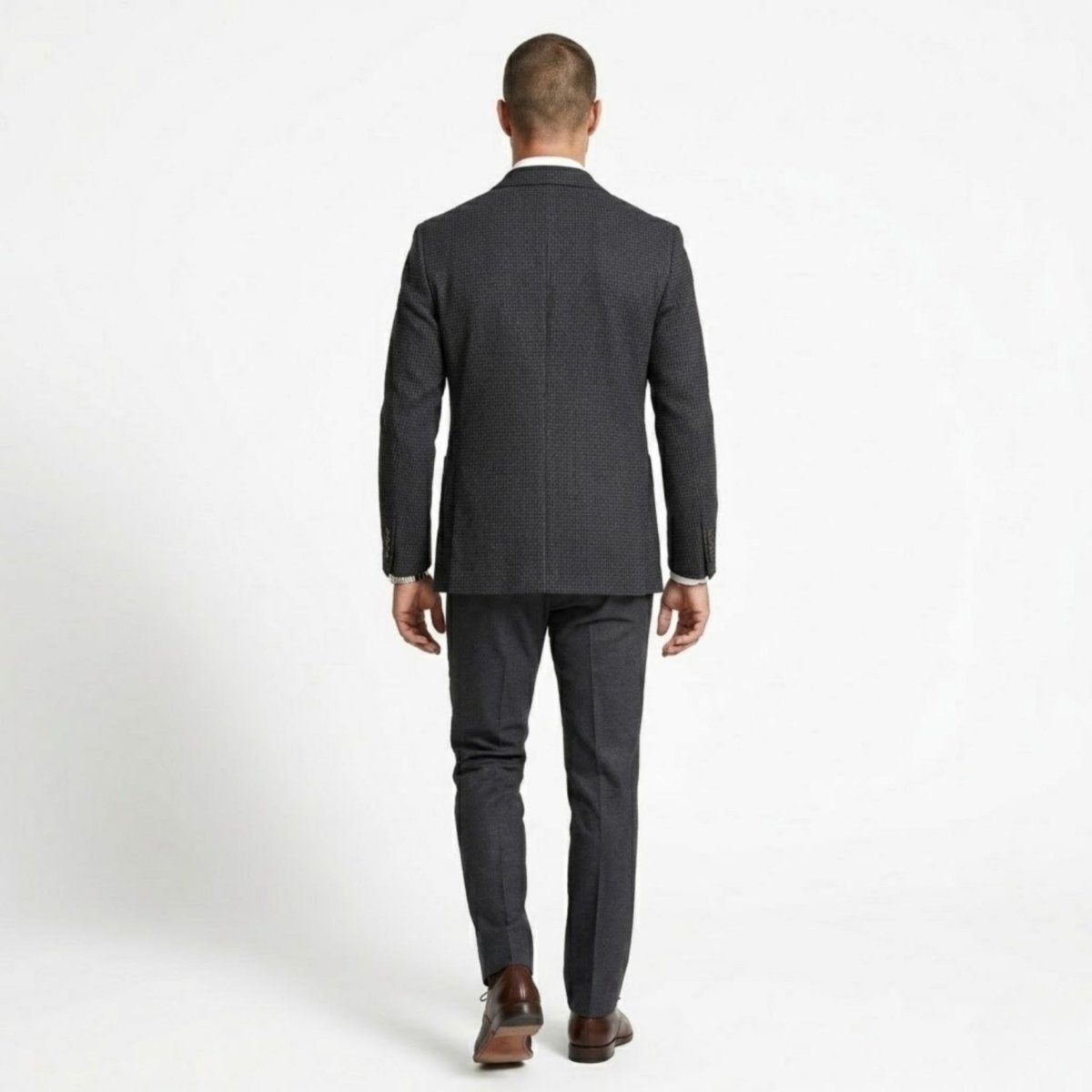 Full body back view of a man walking away wearing a tailored plaid suit jacket and grey trousers.