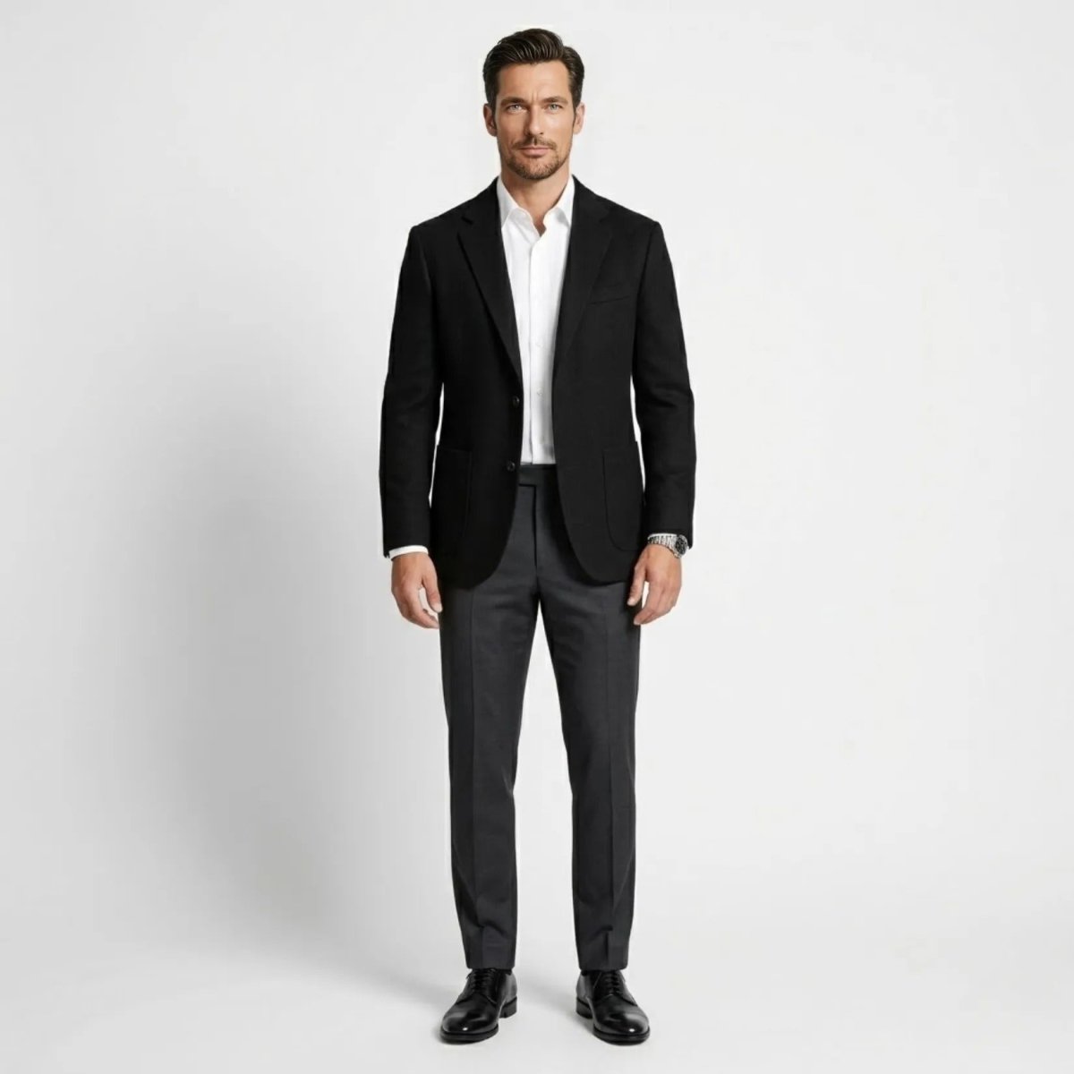 Full body look of men's black smart casual blazer styled with charcoal grey trousers and black dress shoes.