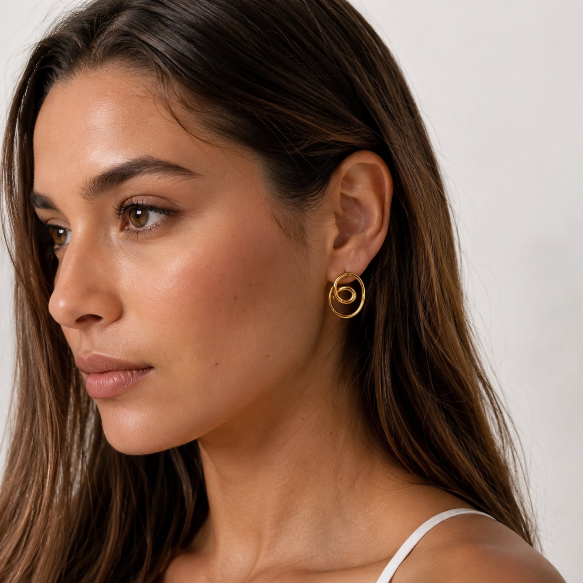 Profile of a beautiful woman wearing gold intertwined loop knot statement stud earrings, illustrating everyday luxury and modern styling.