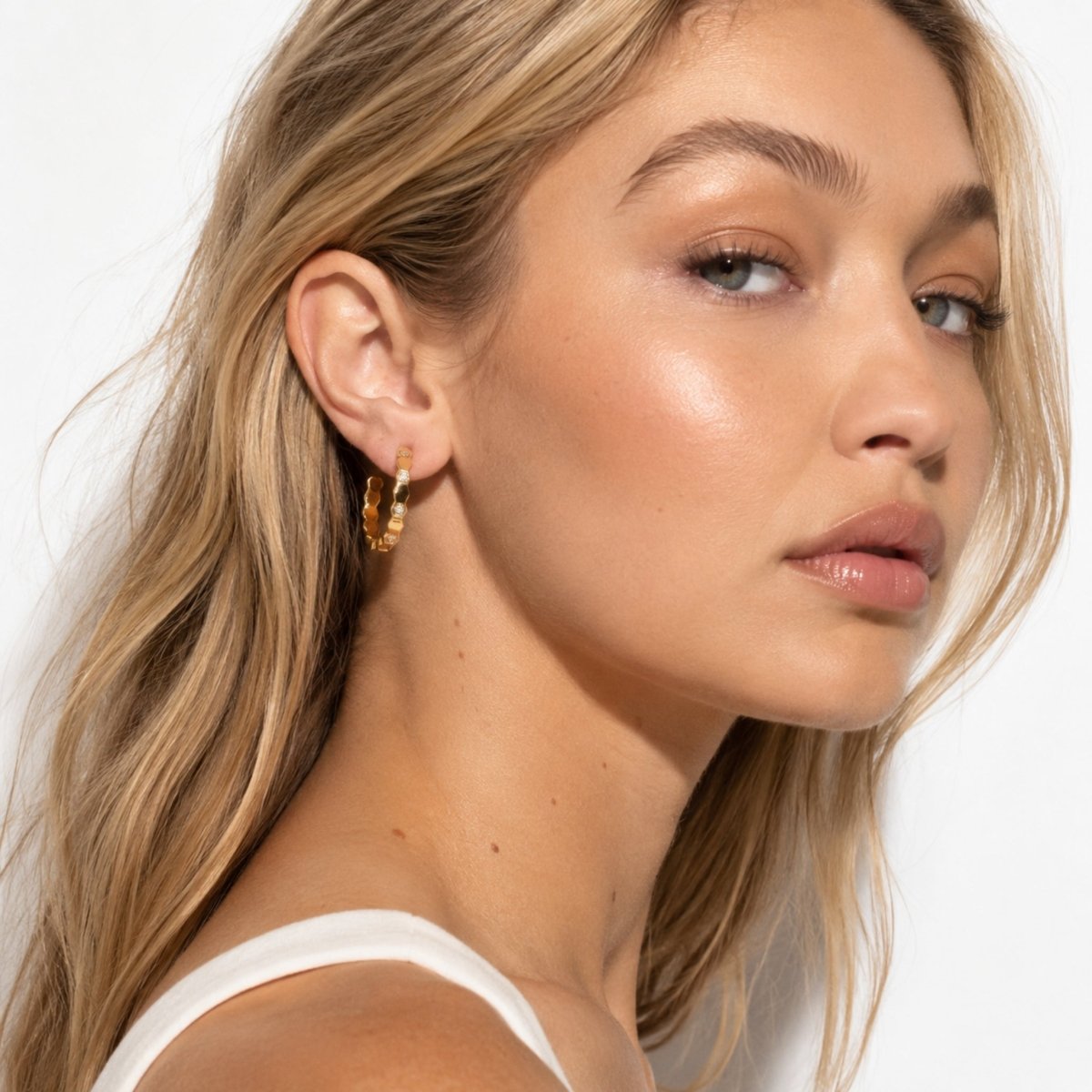 Close up side profile of a blonde female model elegantly wearing Kouvr gold geometric crystal accent hoop earrings