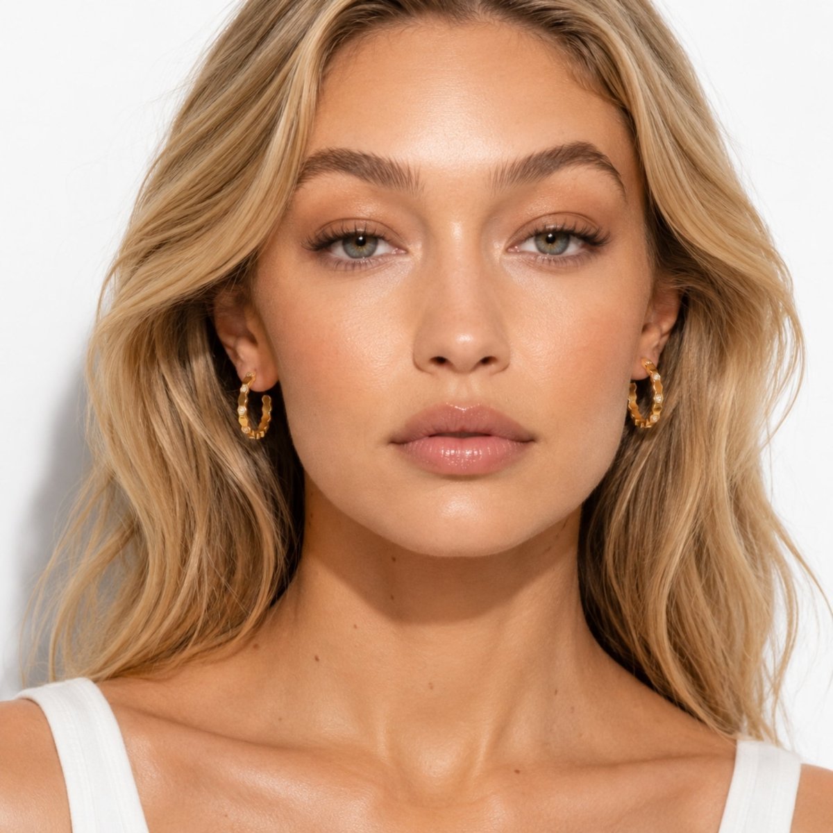 Front facing beauty portrait of a woman styling Kouvr gold geometric crystal hoop earrings with a minimal white ribbed tank top