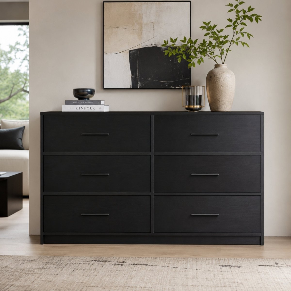Modern black 6-drawer dresser styled in a bright living room with abstract art and a ceramic vase, showcasing matte metal handles and engineered wood grain texture.