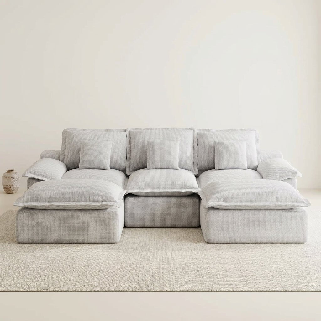 Bright, modern living room featuring a light grey modular sectional sofa, a round stone coffee table, and large window views.
