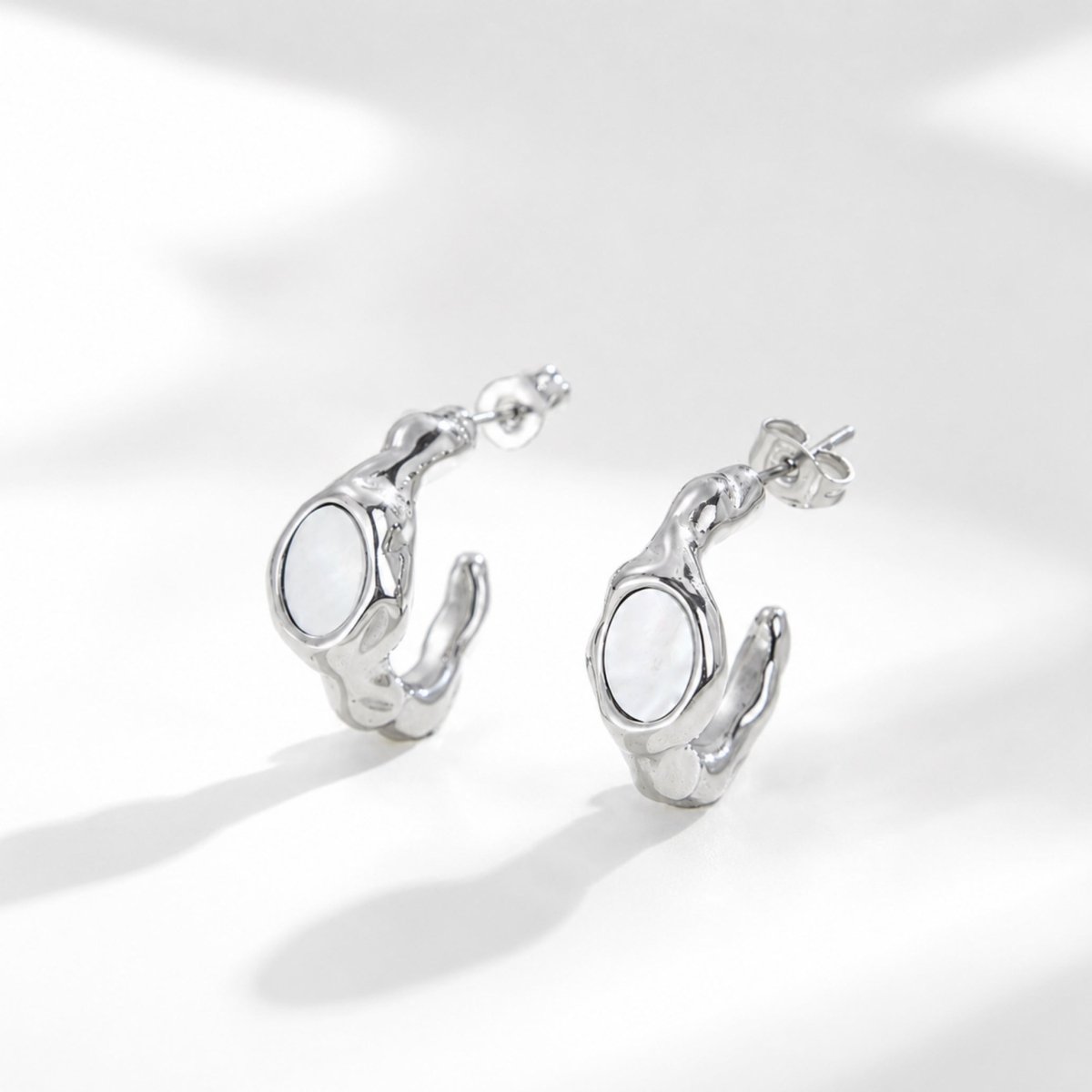 Pair of high polish silver molten chunky hoop earrings featuring an oval mother of pearl inlay against a bright white background.