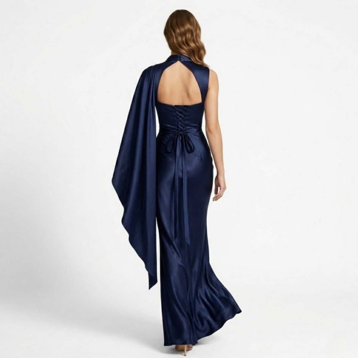 Back view of female model wearing the Kouvr navy blue satin formal gown highlighting the open back cutout and adjustable corset lace-up tie closure.