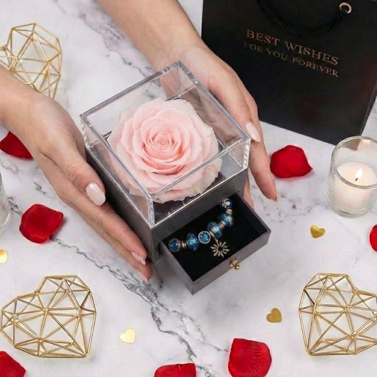 Woman's hands presenting a soft pink eternal rose box with a hidden jewelry drawer containing a silver and blue charm bracelet.