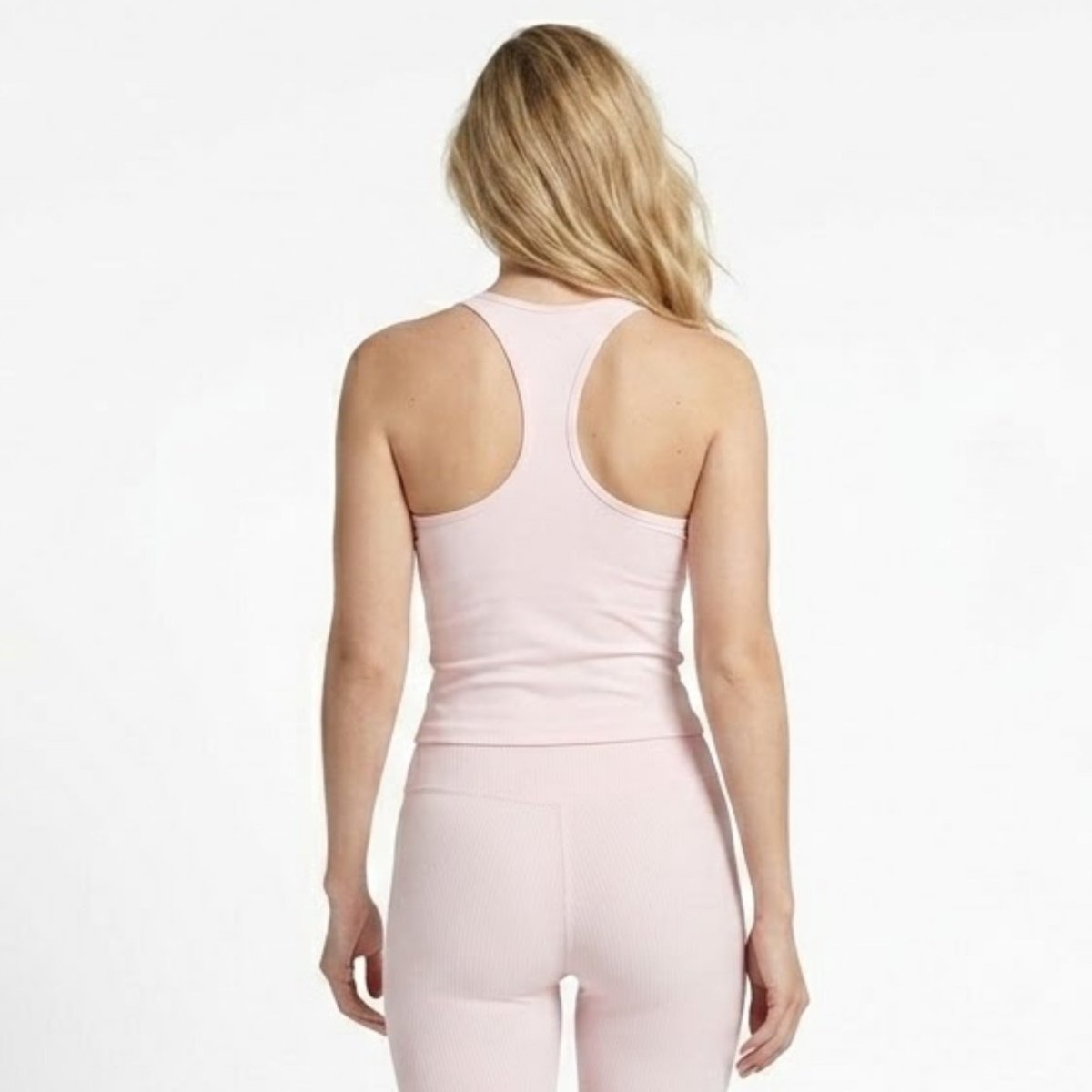Back view of woman modeling form-fitting pale pink athletic leggings and racerback sports camisole.