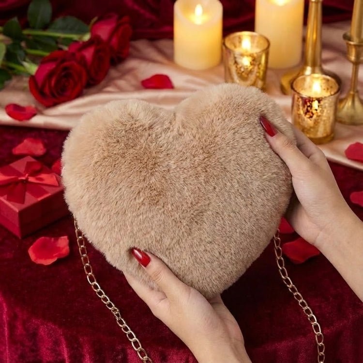 Close-up detail shot of the soft, brown faux fur texture of a heart-shaped purse held by a woman with red nails against a romantic, candlelit red velvet background.
