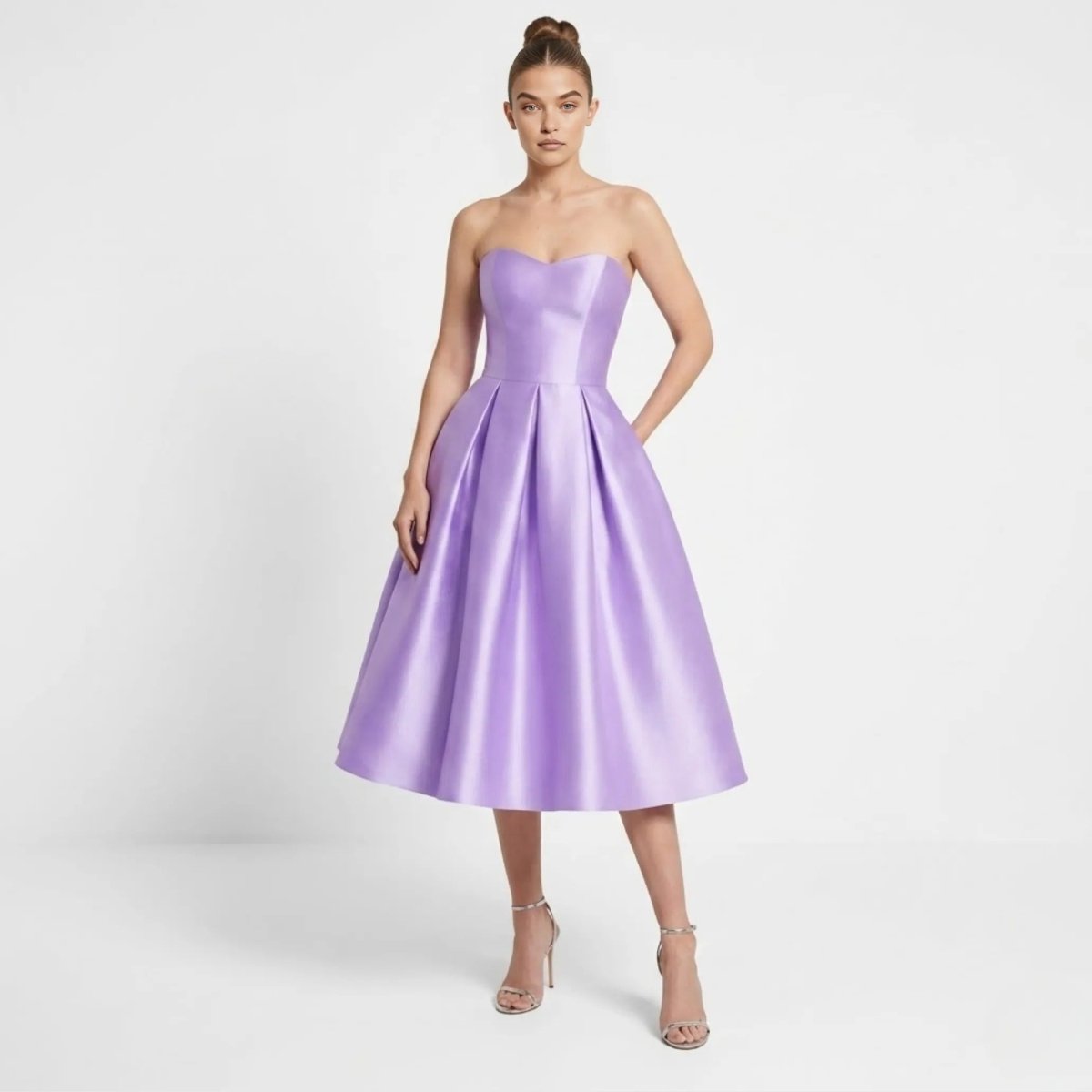 Front view of the Kouvr purple satin strapless pleated midi dress with pockets worn by a model in silver heels.