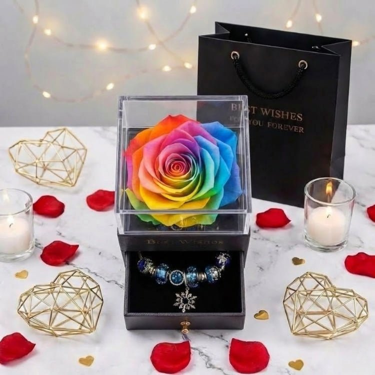 Top-down view of a vibrant rainbow preserved rose gift box styled with candles and gold hearts, featuring a drawer with a snowflake charm bracelet.