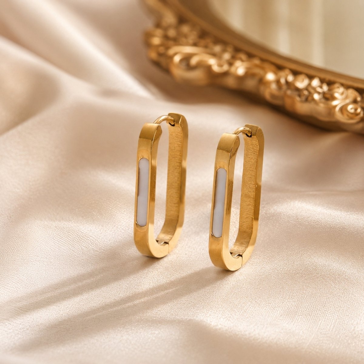 Close up studio shot of contemporary silver rectangular hoop earrings with a sleek white inlay standing upright against a white background.