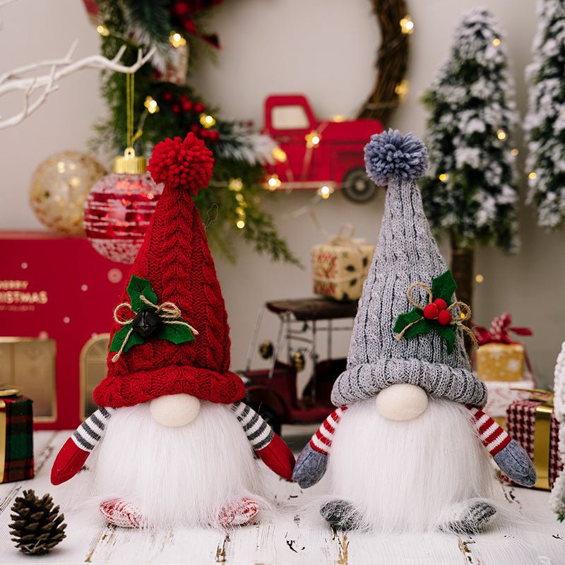 A pair of grey and red Scandinavian Christmas gnomes with a long white beard and knit hat with a pompom, sitting on a white wooden table surrounded by wrapped presents.