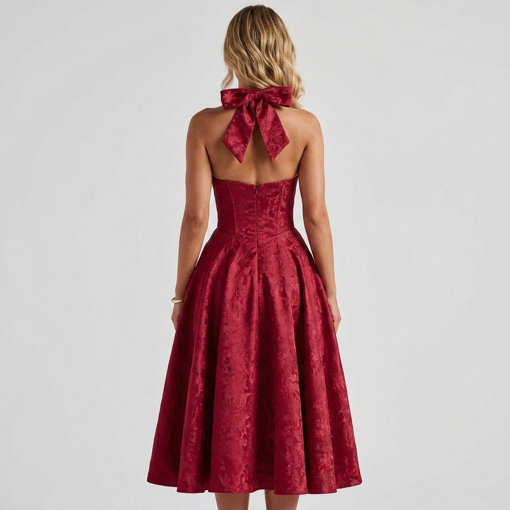 Back view of a woman wearing the Kouvr red jacquard formal dress highlighting the open back design, large dramatic neck bow, and flared A-line skirt.