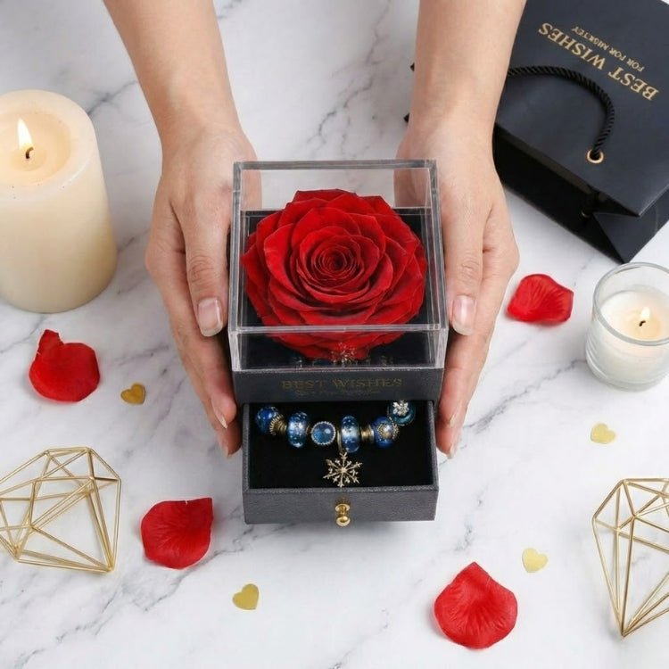 Hands holding a red eternal rose jewelry box, showcasing the preserved flower under a clear lid and a charm bracelet in the bottom compartment.
