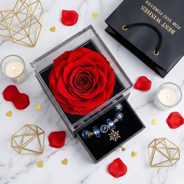 Top-down view of a large red preserved rose inside a black gift box, styled with candles and red petals for a romantic Valentine's setting.