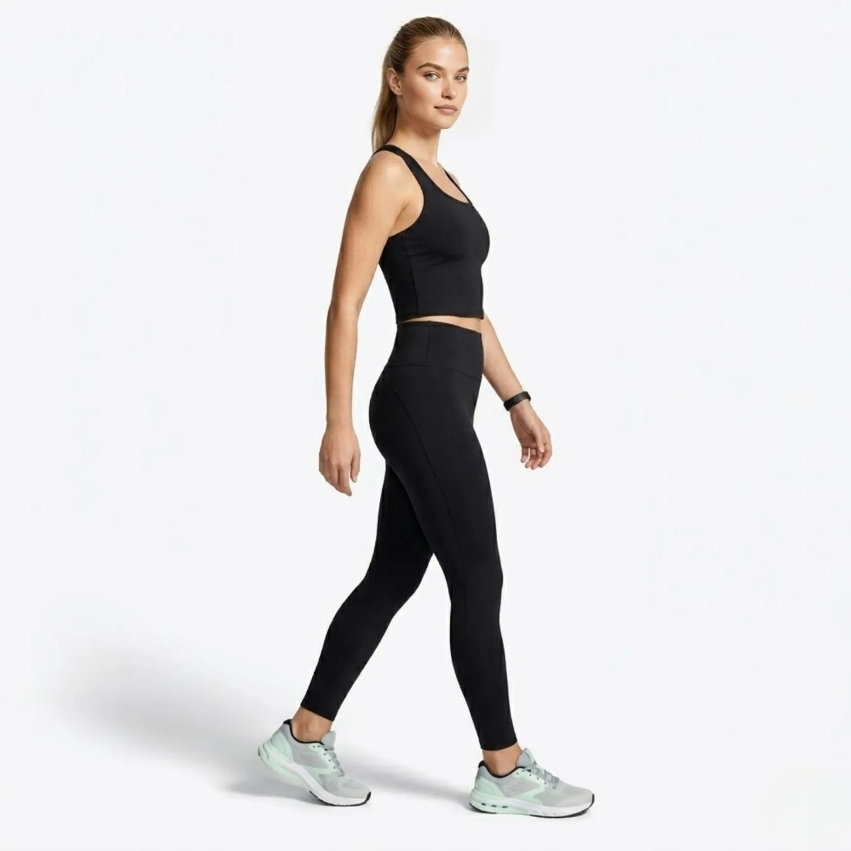 Side profile of model walking in Kouvr form-fitting black workout tank top and performance leggings.