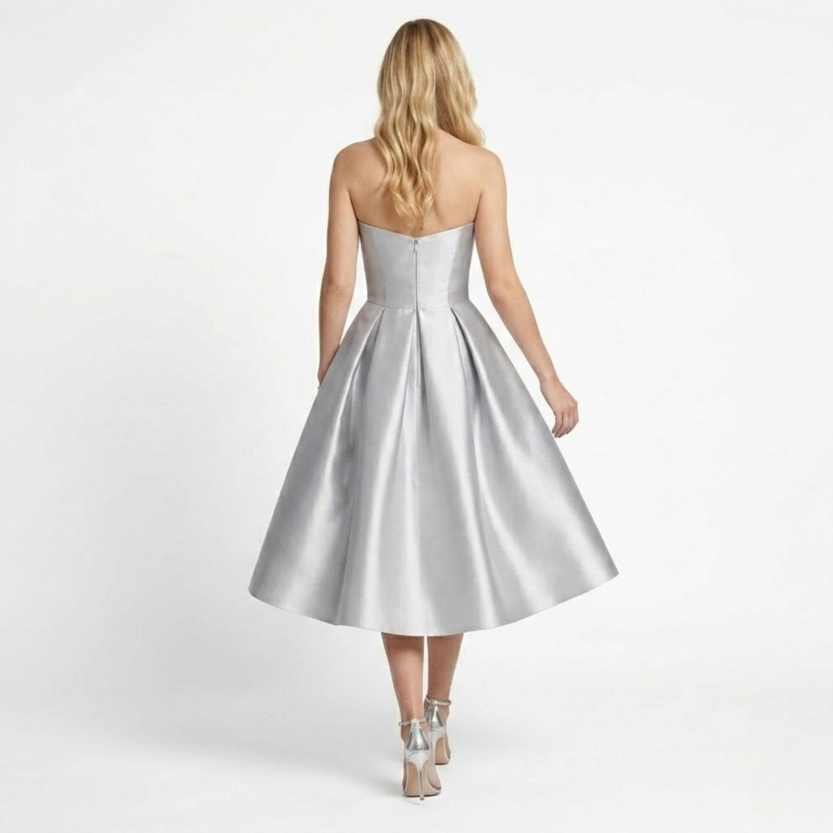 Back view of a silver strapless midi dress showing invisible back zipper and deep pleat details on the model.