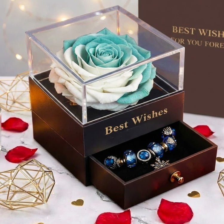 Angled close-up of a teal and white preserved rose bloom in a clear acrylic box, featuring a snowflake charm bracelet in the open drawer.