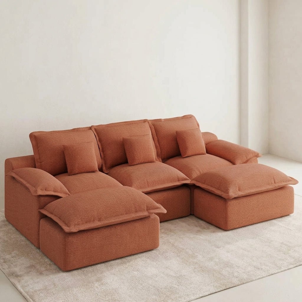 Terracotta modular sectional sofa with plush cushions and ottomans in a bright, sunlit living room with a fireplace.
