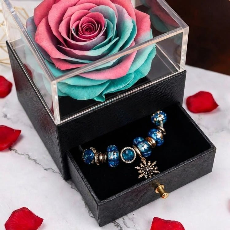 Close-up of a pink and turquoise two-tone eternal rose with a jewelry drawer pulled open to reveal a blue bead charm bracelet.