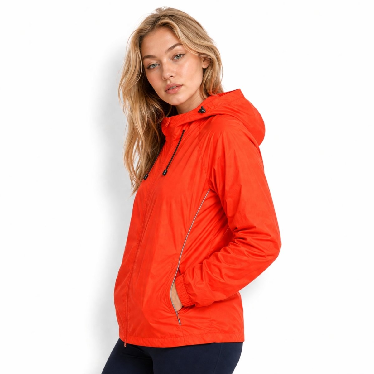Side profile of woman in Kouvr neon orange athletic shell jacket highlighting the high-visibility reflective piping along the sleeve seams.