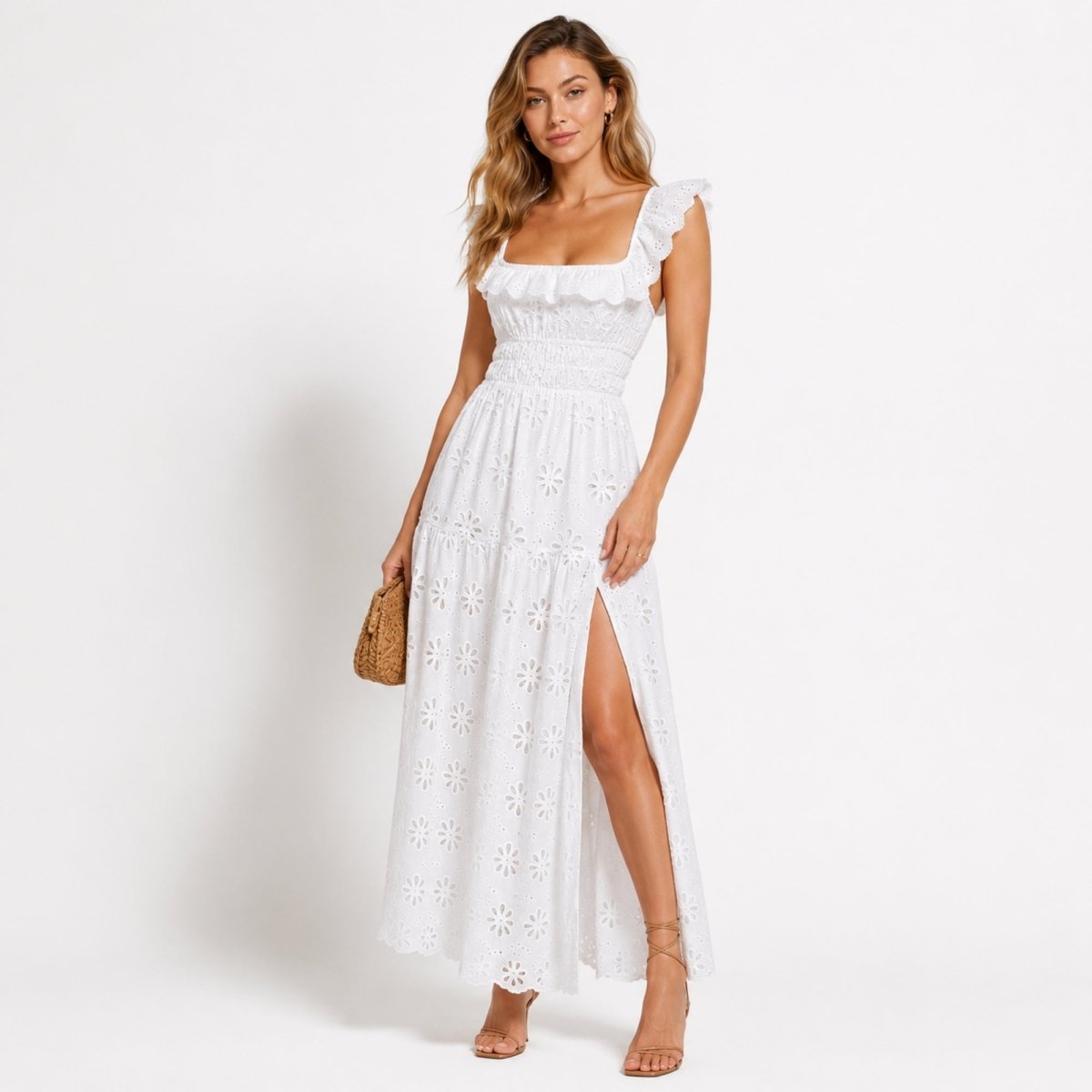 Woman wearing Kouvr white eyelet lace maxi dress with high side slit and ruffle square neckline, holding a woven clutch handbag.