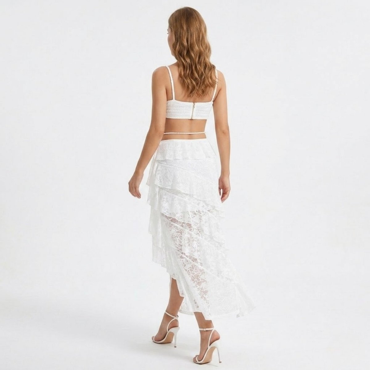 Back view of the Kouvr white two piece outfit featuring an exposed top zipper and a flowing high-low lace skirt.