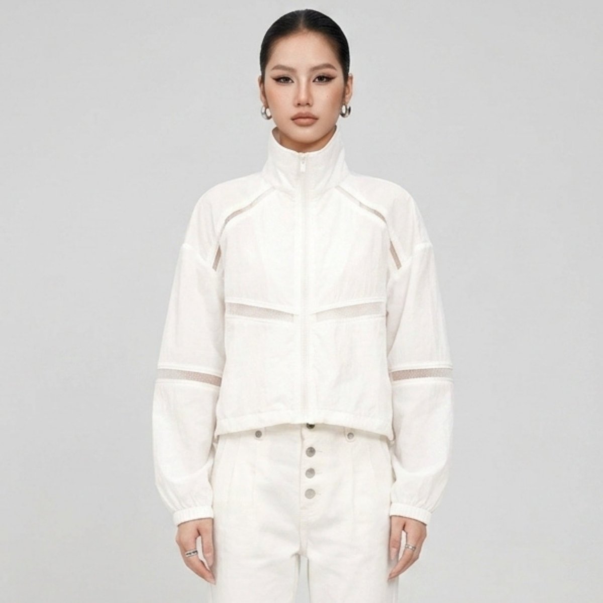Front view of a woman wearing the Kouvr white mesh panel cropped track jacket and white pants