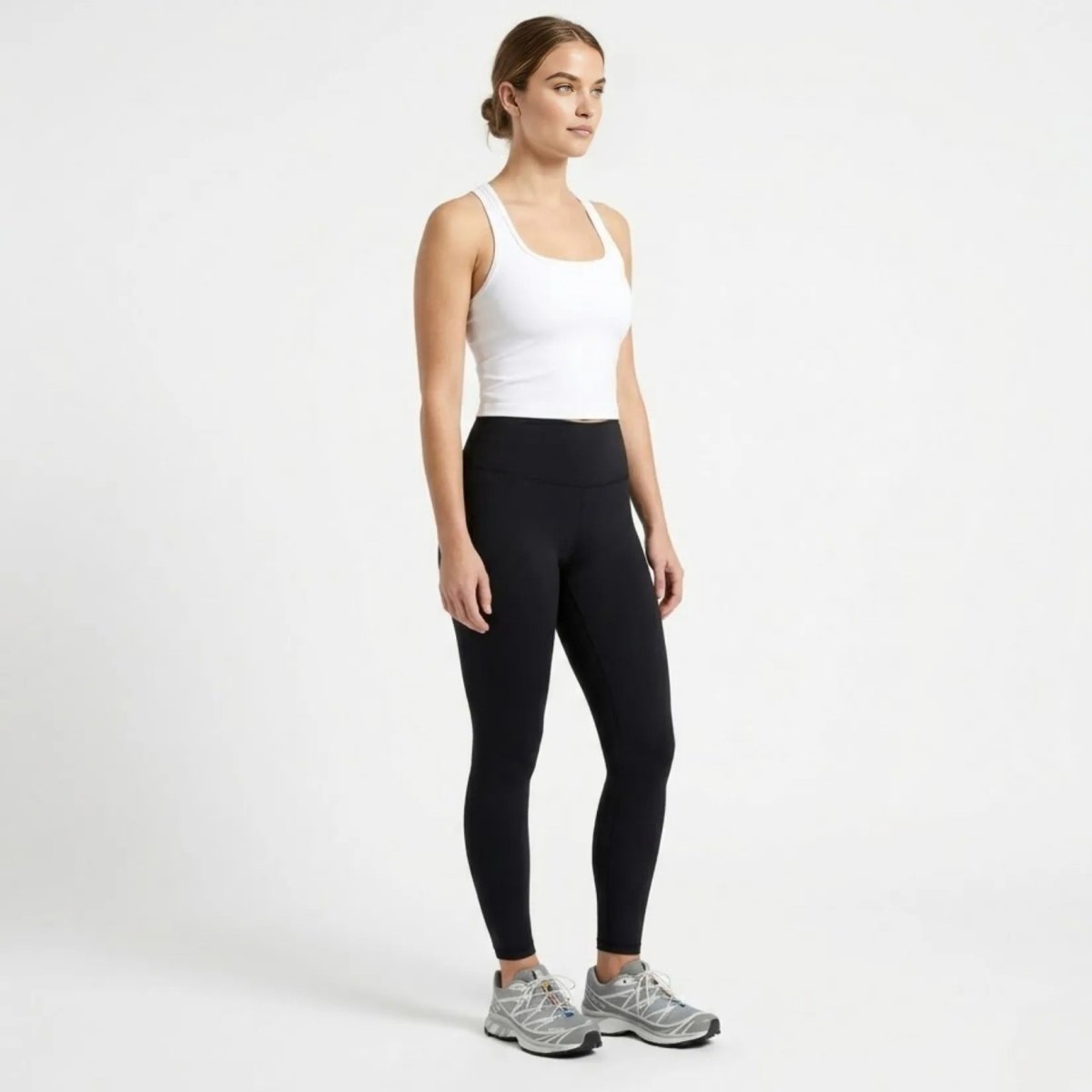 Side profile of female model wearing a white seamless cropped gym tank top and black athletic tights.