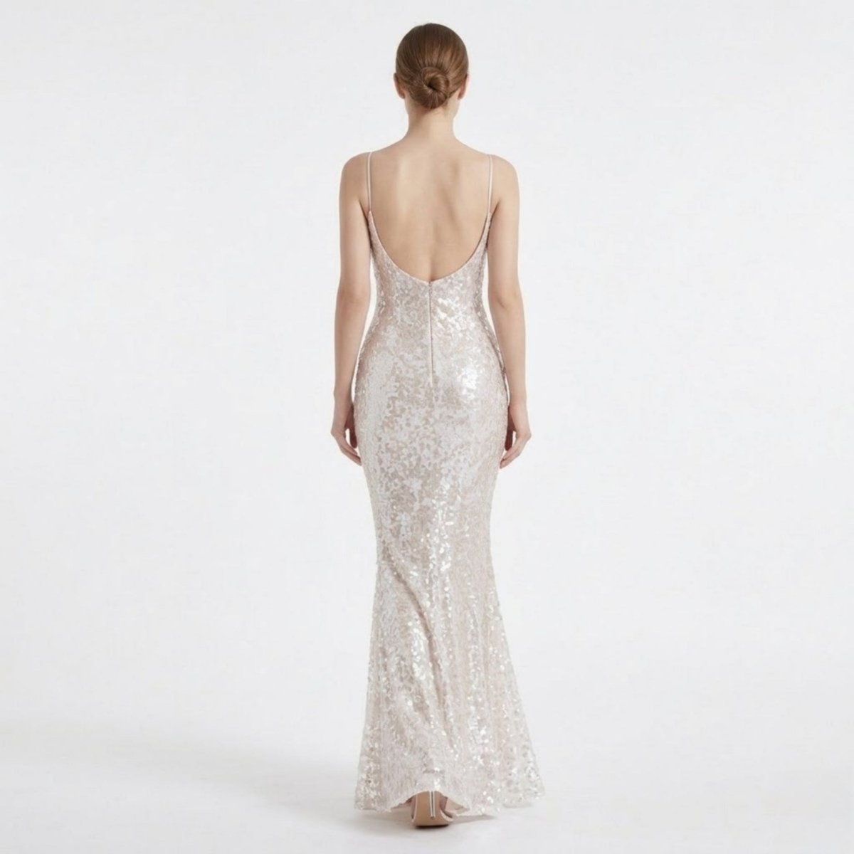 Back view of a female model wearing a backless white sequin formal dress, highlighting the deep V open back design and mermaid skirt flare.